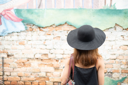 Fototapeta Naklejka Na Ścianę i Meble -  Young hipster is standing at the sight of the beauty of art written on the old vintage red brick wall while traveling in Chanthaburi, Thailand Province on a holiday.