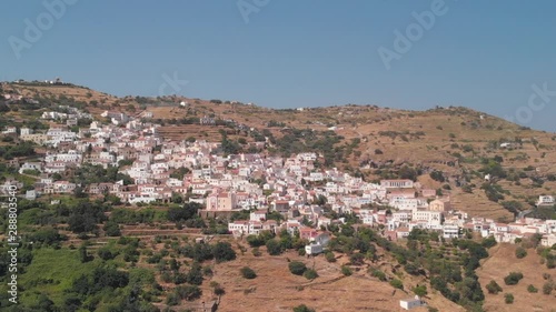 Forwards aerial towards Ioulida village on Kea Island, Greece. Perched on hill against blue sky CROP photo