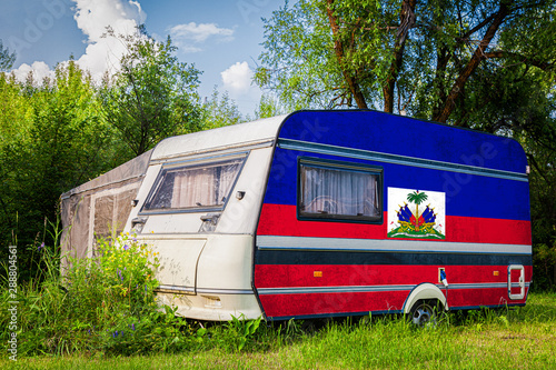 A car trailer, a motor home, painted in the national flag of  Haiti stands parked in a mountainous. The concept of road transport, trade, export and import between countries.