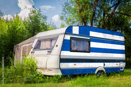 A car trailer, a motor home, painted in the national flag of  Greece stands parked in a mountainous. The concept of road transport, trade, export and import between countries.