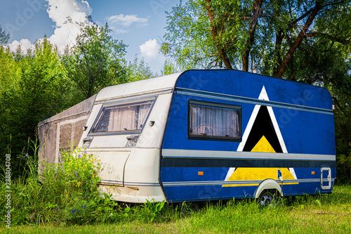 A car trailer, a motor home, painted in the national flag of  Saint lucia stands parked in a mountainous. The concept of road transport, trade, export and import between countries.