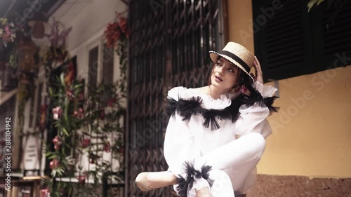 Beautiful and young fashion mestizo girl seating on the bench, at the asian street near old buildings with straw hat . Journey concept in Vietnamese tourist destination in Hanoi. 