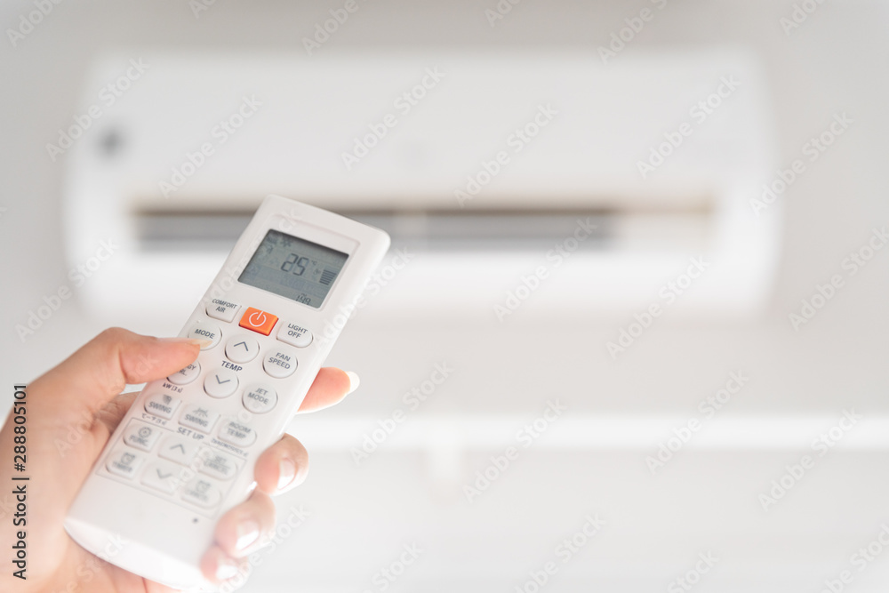 woman hand holding remote controller directed on the air conditioner inside the room and set at ambient temperature,25 degrees celsius. woman hand holding remote controller directed on the air conditioner inside the room and set at ambient temperature,25 degrees celsius.