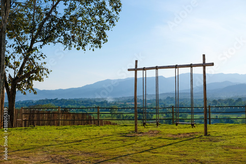 Empty wooden swing on children playground with field and mountain landscape background