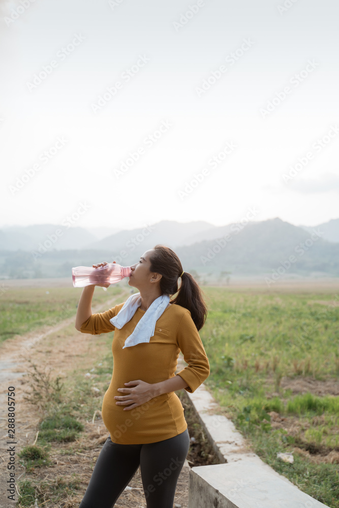 thirsty pregnant woman after workout drinking a bottle of water thirsty pregnant woman after workout drinking a bottle of water