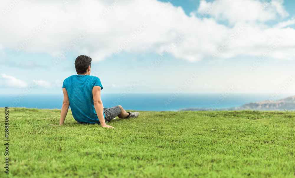 Man sitting on a hill over looking the ocean.