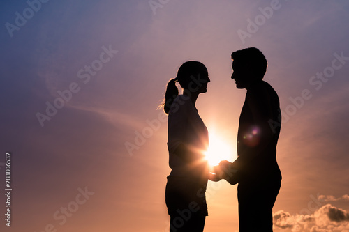 Man woman sunset silhouette holding hands smiling and looking into each others eyes with love. 