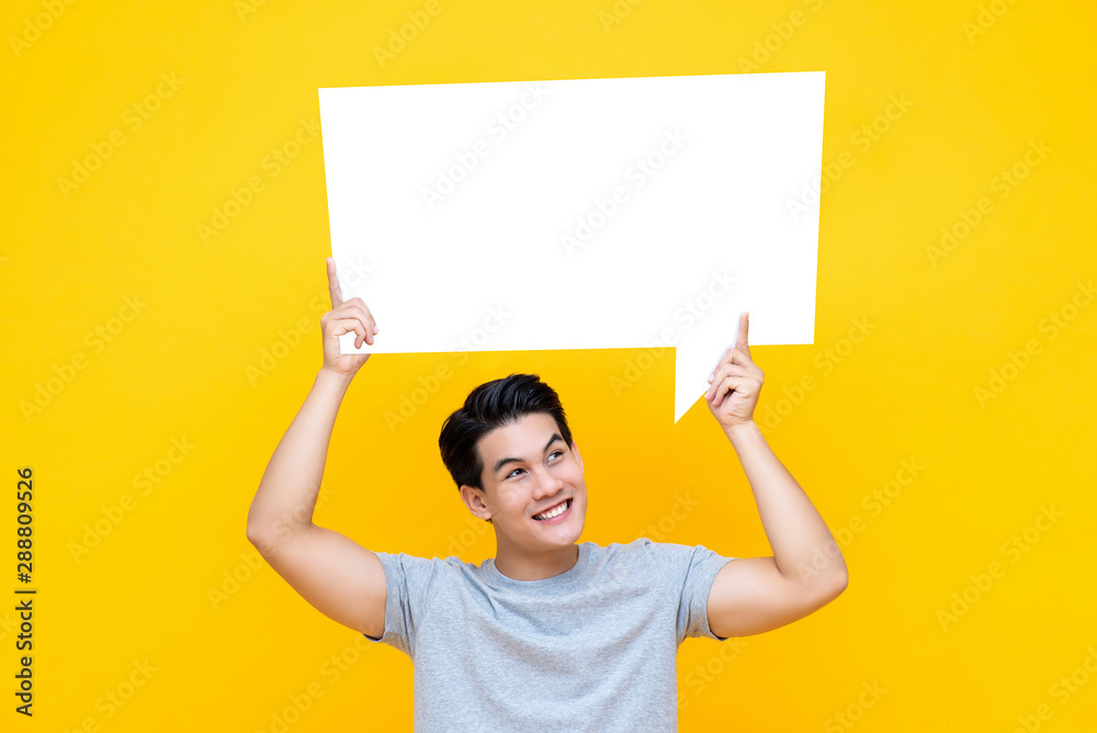 Happy smiling young handsome Asian man holding speech bubble Happy smiling young handsome Asian man holding speech bubble