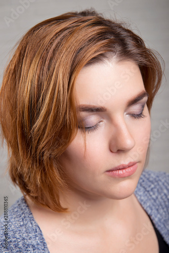 Evening make-up on the closed eyes of a red-haired girl close-up.