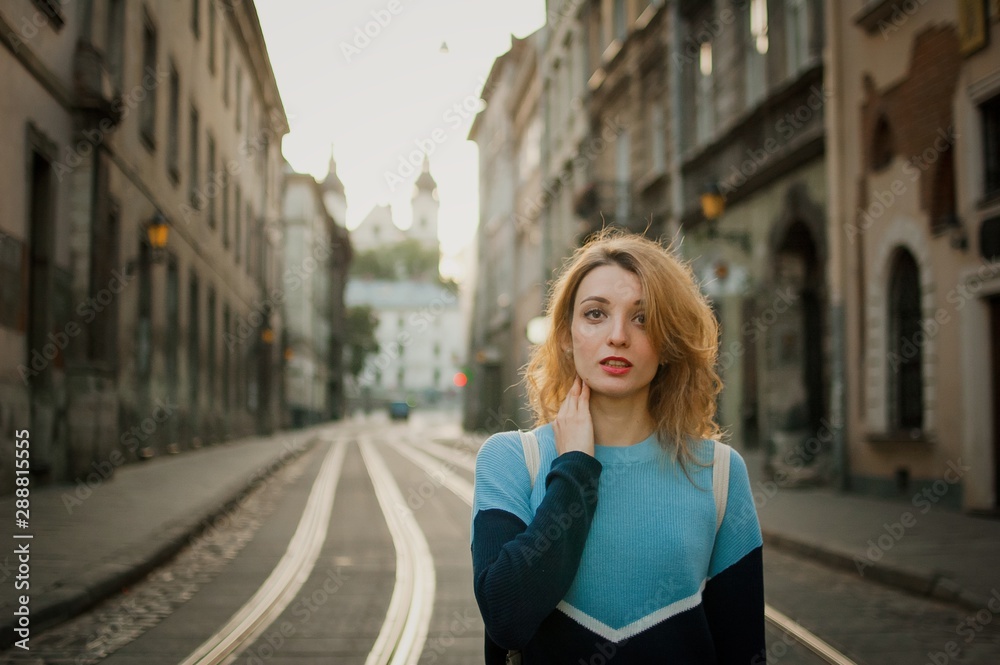 Front view of young adult girl tourist enjoying her trip early in the morning in ancient city in Europe on empty street with tramway background.