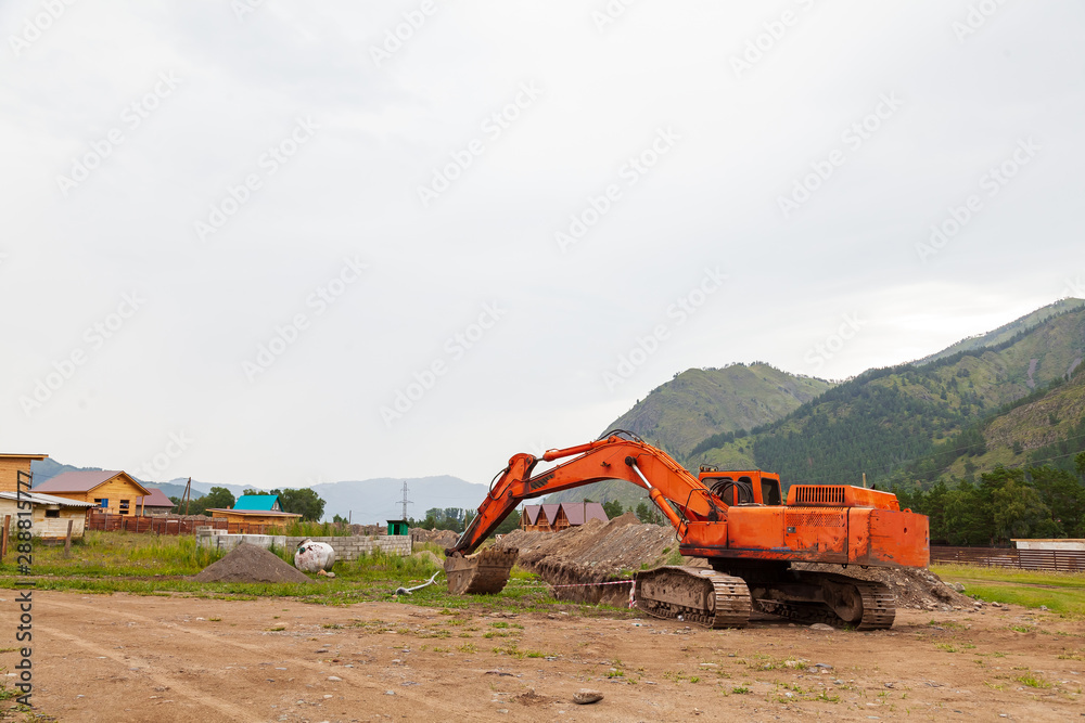 Large orange excavator with a lowered bucket during repair work in the mountains on a summer day. Large orange excavator with a lowered bucket during repair work in the mountains on a summer day.