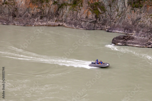 Aerial view of a gray rubber motor boat sailing on a green river in the mountains between rocks and cliff