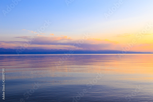 Beautiful sunset on a lake in the mountains. Kyrgyzstan, Issyk-Kul Lake. Bright sky, background in warm colors. © Alwih
