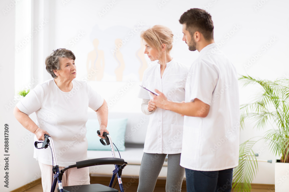 Obraz premium Grey senior lady with walker during physiotherapy with professional female doctor and male nurse