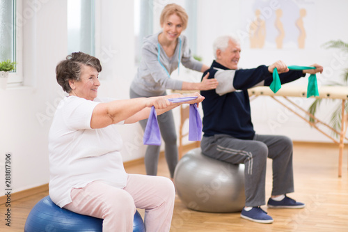 Elderly man and woman exercising on gymnastic balls during physiotherapy session at hospital