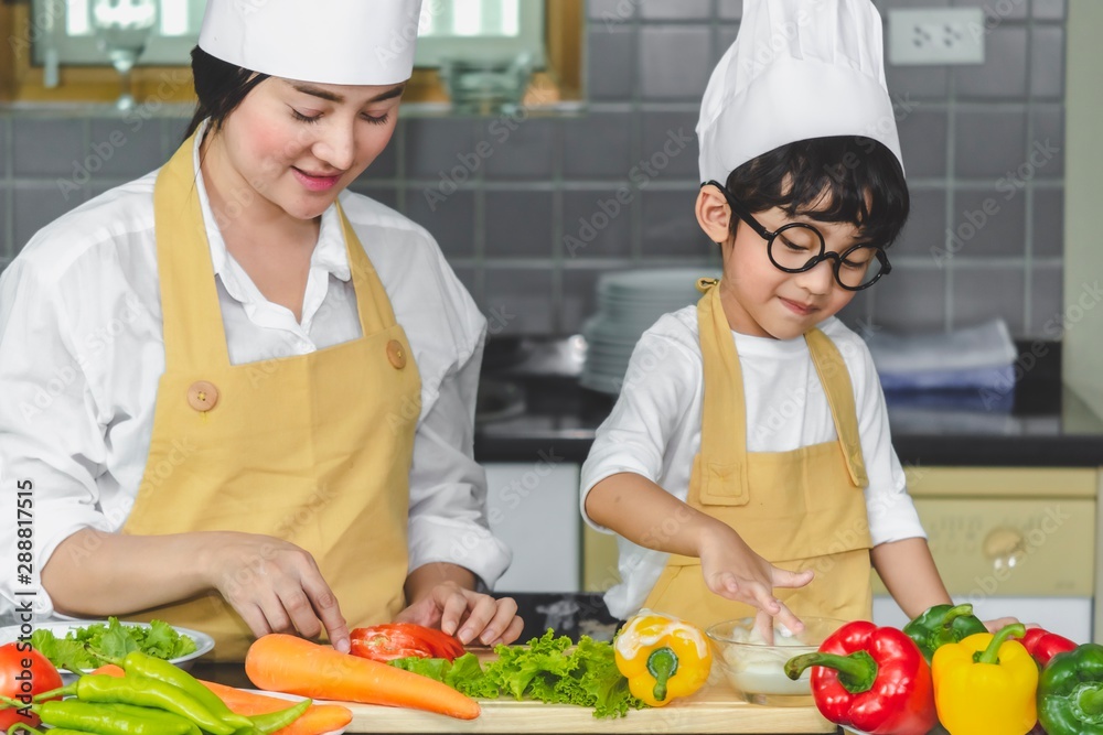 Asian woman young mother with son boy cooking salad mom sliced vegetables food son tasting salad dressing with vegetable carrots and tomatoes, bell peppers for happy family cook food enjoyment kitchen