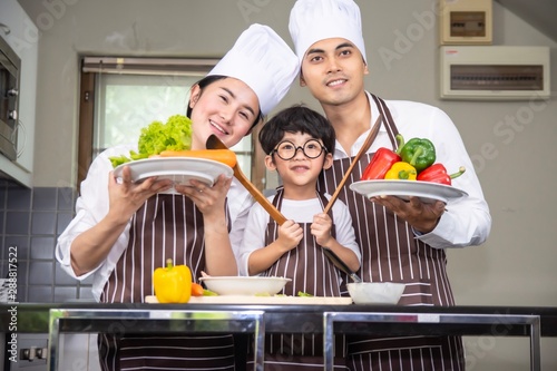  Asian woman young mother and father with son boy cooking salad food with vegetable holding tomatoes and carrots, bell peppers on plate for happy family cook food enjoyment lifestyle kitchen in home