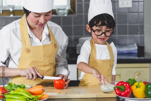 Asian woman young mother with son boy cooking salad mom sliced vegetables food son tasting salad dressing with vegetable carrots and tomatoes, bell peppers for happy family cook food enjoyment kitchen