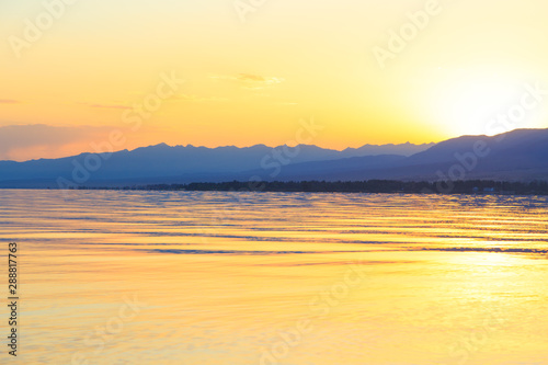 Beautiful sunset on a lake in the mountains. Kyrgyzstan, Issyk-Kul Lake. Bright sky, background in warm colors.