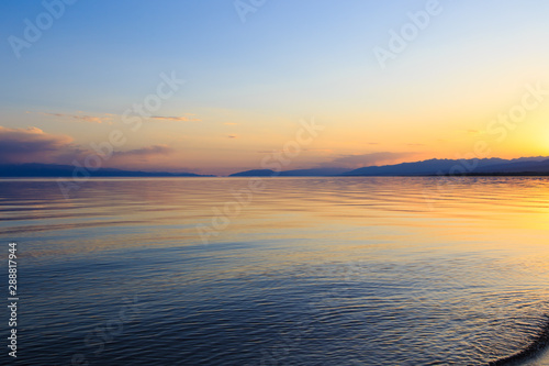 Beautiful sunset on a lake in the mountains. Kyrgyzstan, Issyk-Kul Lake. Bright sky, background in warm colors.