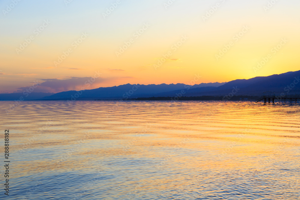 Obraz premium Beautiful sunset on a lake in the mountains. Kyrgyzstan, Issyk-Kul Lake. Bright sky, background in warm colors.
