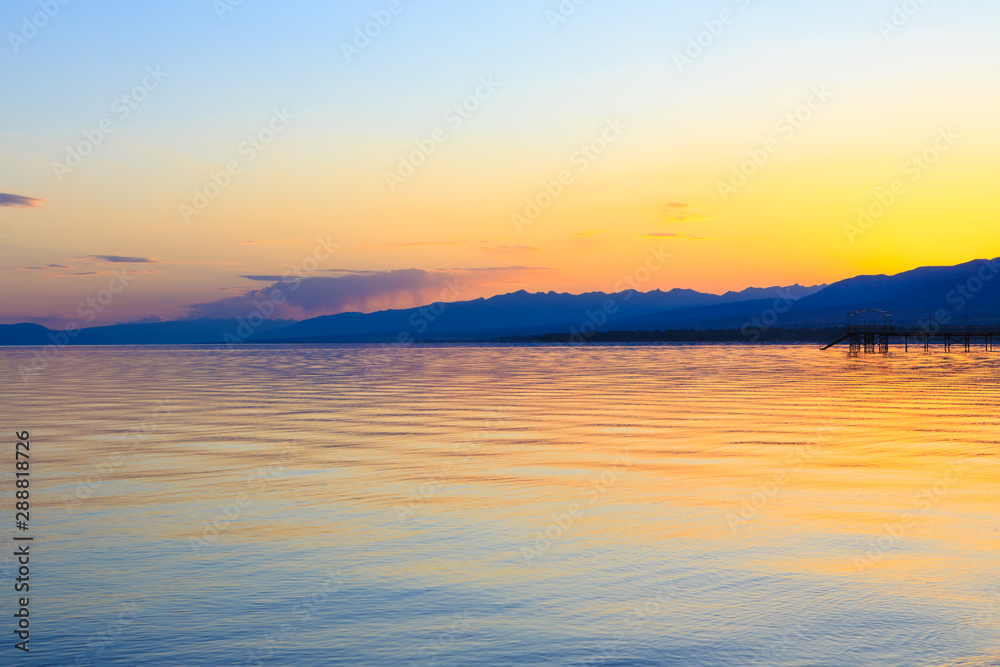 Beautiful sunset on a lake in the mountains. Kyrgyzstan, Issyk-Kul Lake. Bright sky, background in warm colors. Beautiful sunset on a lake in the mountains. Kyrgyzstan, Issyk-Kul Lake. Bright sky, background in warm colors.
