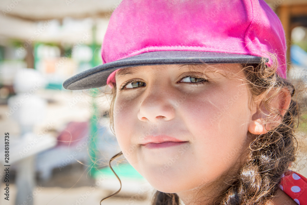 In summer, on a bright sunny day, a little girl in a swimsuit and cap sits on the beach. In summer, on a bright sunny day, a little girl in a swimsuit and cap sits on the beach.