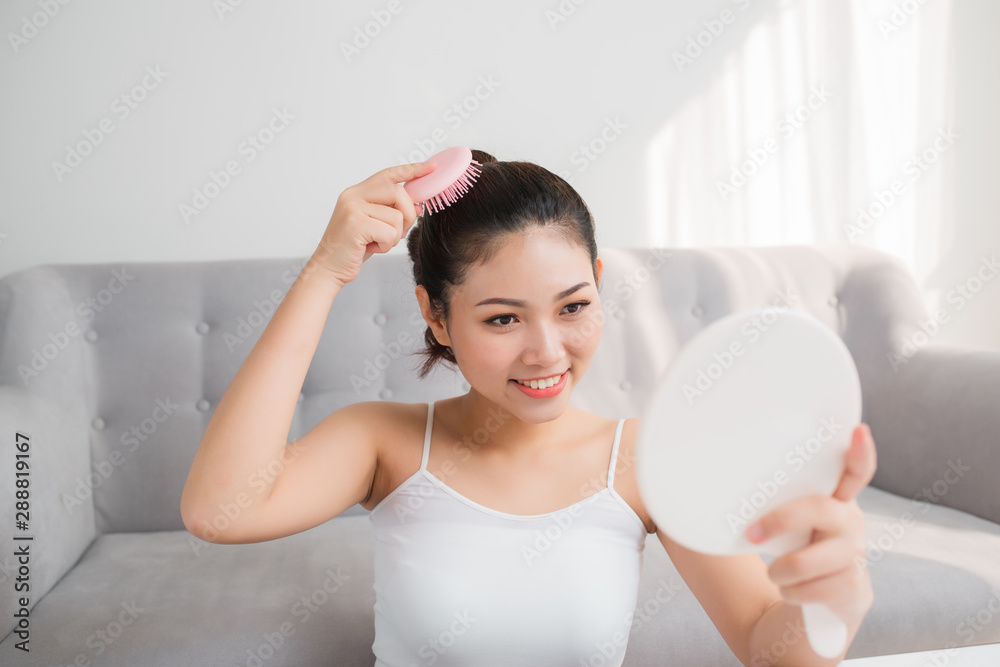 Portrait of beautiful young woman combing her hair, looking mirror Portrait of beautiful young woman combing her hair, looking mirror