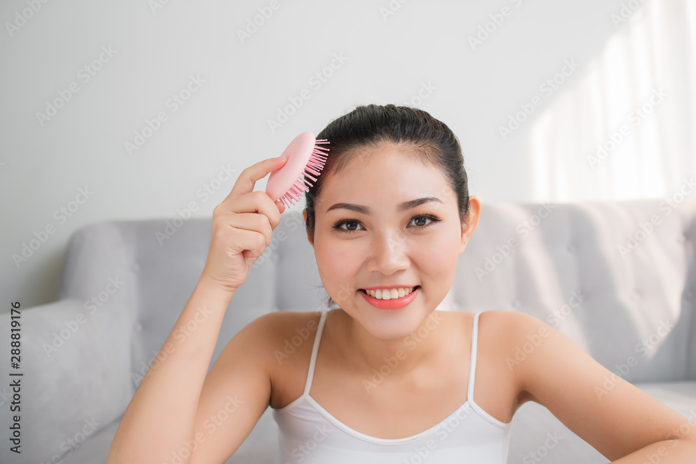 Portrait of beautiful young woman combing her hair, looking at camera and smiling