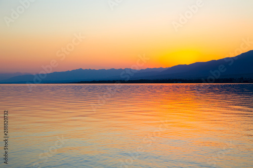Beautiful sunset on a lake in the mountains. Kyrgyzstan, Issyk-Kul Lake. Bright sky, background in warm colors. © Alwih