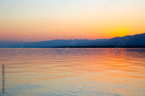 Beautiful sunset on a lake in the mountains. Kyrgyzstan  Issyk-Kul Lake. Bright sky  background in warm colors.