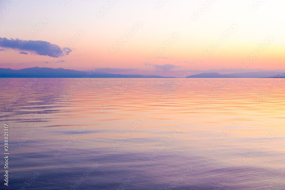 Beautiful sunset on a lake in the mountains. Kyrgyzstan, Issyk-Kul Lake. Bright sky, background in warm colors.