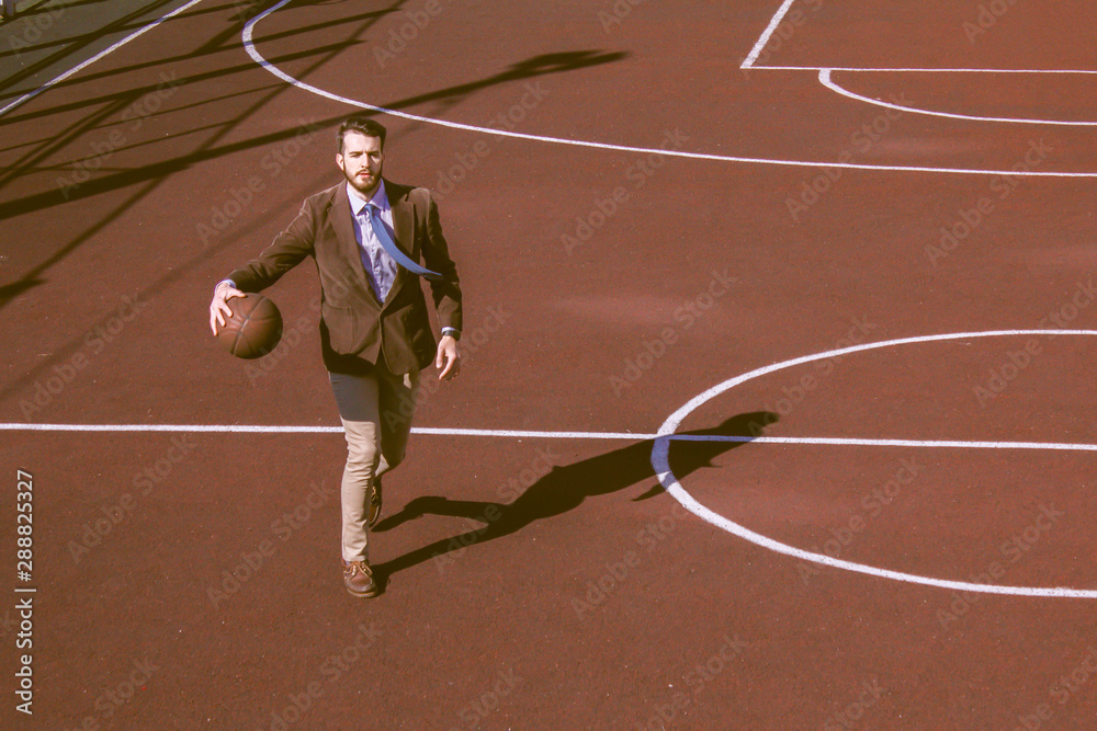 Young handsome bearded guy. Businessman in a suit outside work plays basketball on the playground. Fashionable man in a tie, concept of businessman athlete. Sports lifestyle, break at work. Young handsome bearded guy. Businessman in a suit outside work plays basketball on the playground. Fashionable man in a tie, concept of businessman athlete. Sports lifestyle, break at work.