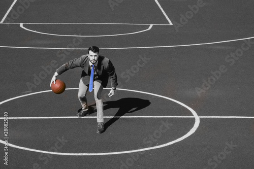 Partial black and white image of a business fashionable bearded hipster businessman playing basketball on the sports field. Color ball and tie. Active lifestyle  business activities during the break.