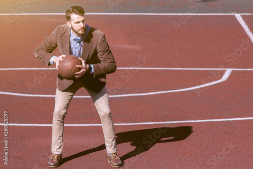Attractive stylish bearded guy in a tie and jacket on the sports basketball court. A businessman goes in for sports and leads an active lifestyle. Sports break office worker. Lifestyle business man. © Daniil