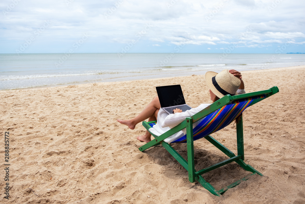 A woman using and typing on laptop computer while lying down on a beach chair