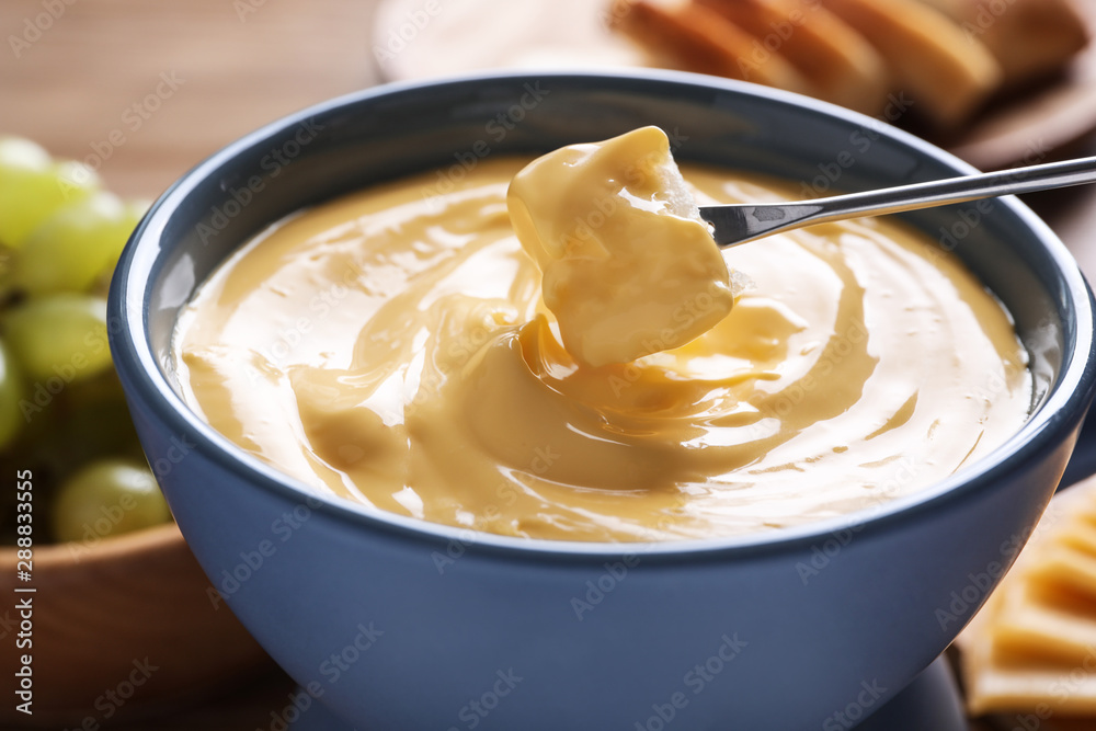 Dipping bread into pot with cheese fondue on table, closeup Dipping bread into pot with cheese fondue on table, closeup