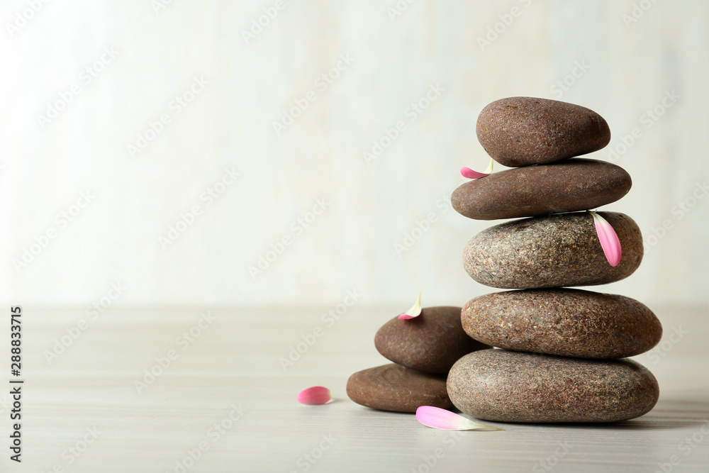 Stack of spa stones and petals on table against white background, space for text Stack of spa stones and petals on table against white background, space for text