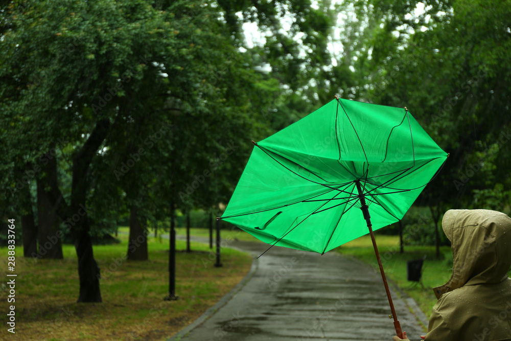 Woman with broken green umbrella in park on rainy day