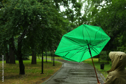 Woman with broken green umbrella in park on rainy day