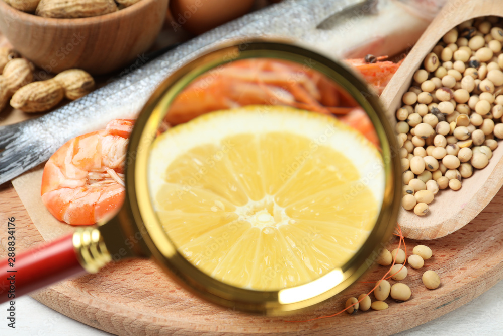 Different products with magnifier focused on lemon and shrimps, closeup. Food allergy concept Different products with magnifier focused on lemon and shrimps, closeup. Food allergy concept