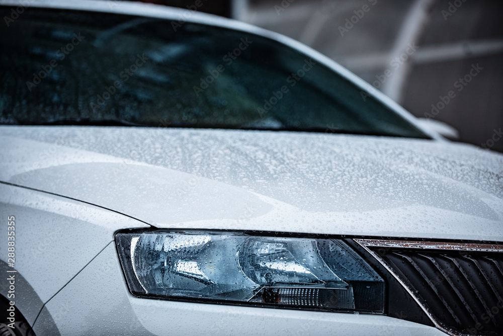 view of the front of a white car with water drops after rain. Concept on the topic of polishing a car.