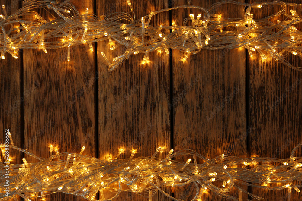 Glowing Christmas lights on wooden background, top view. Space for text