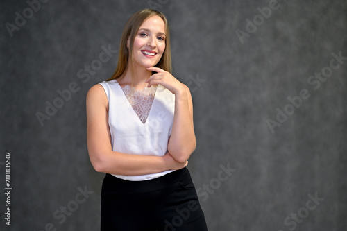 Business photo portrait of a young woman in a business suit on a gray background. Well-groomed hair, slim figure. It is in different poses.