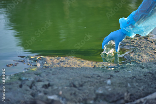 Close-up environmentalist hand of a researcher in a process of taking a sample of contaminated water from a lake photo