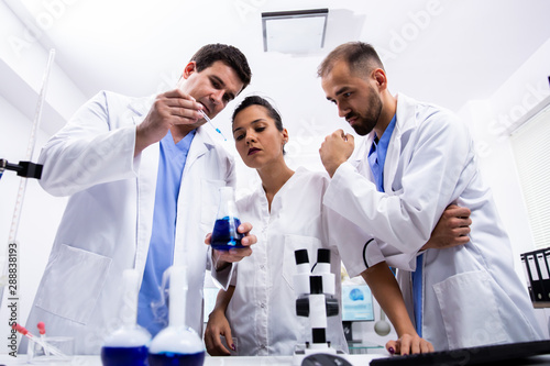 Team of scientist in white coat looking at a sample of smoking blue liquid