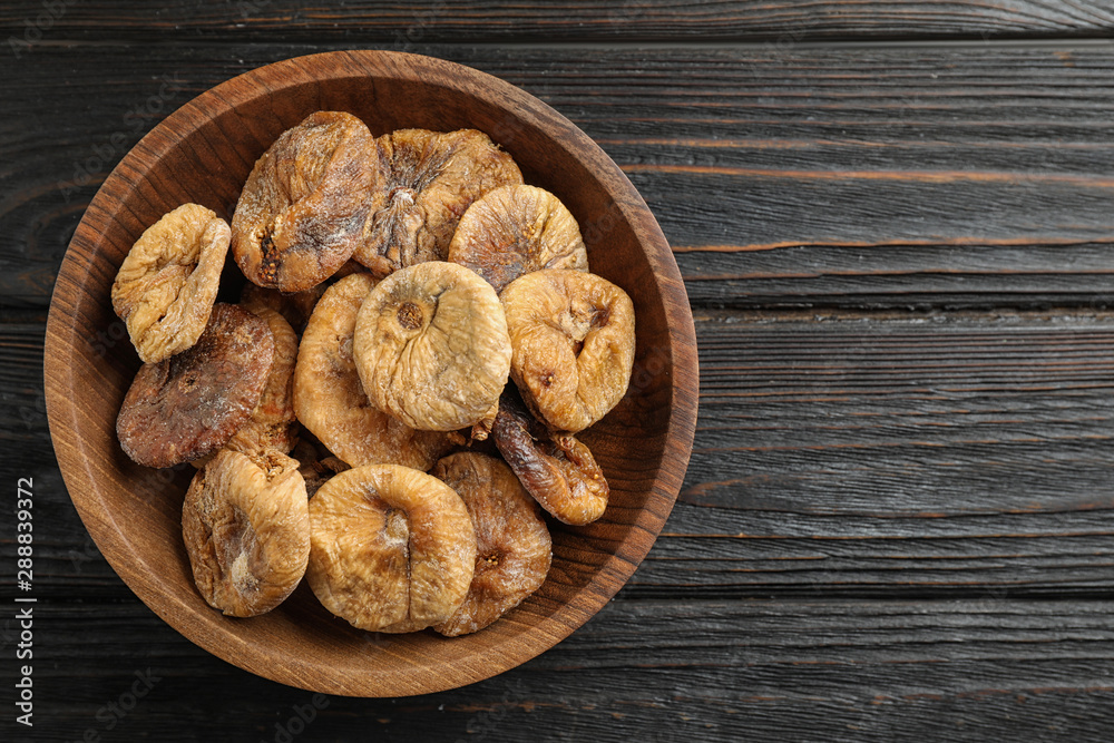 Fototapeta premium Wooden bowl of tasty dried figs on black table, top view. Space for text