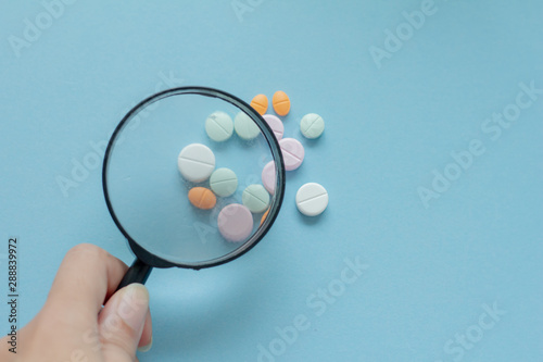 Magnifying glass with pills on blue background. pharmaceutical inspection identifies pills. Medicinal substance quality concept.