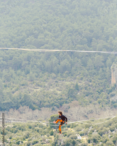 A man is walking along a stretched sling. Highline in the mountains. Man catches balance. Performance of a tightrope walker in nature. Highliner on the background of valley.