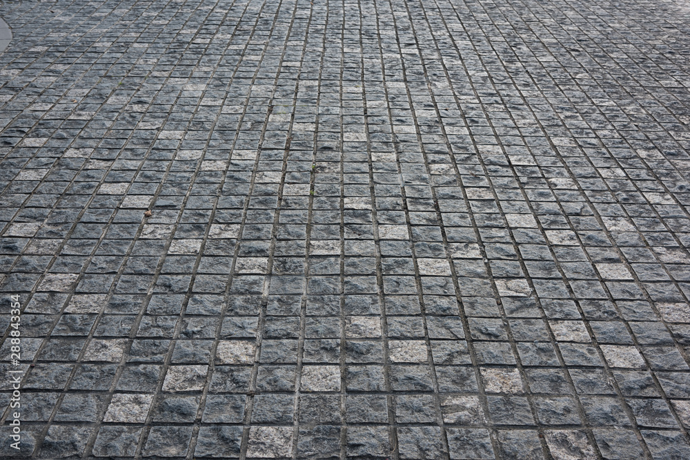 Fototapeta premium Gray square small stone brick paved pavement surface low angle close-up